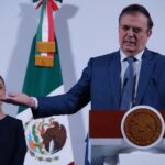 Economy Minister Marcelo Ebrard gestures while standing at a podium as President Claudia Sheinbaum looks on