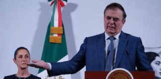 Economy Minister Marcelo Ebrard gestures while standing at a podium as President Claudia Sheinbaum looks on