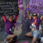 Two protestors wearing purple crouch down and display their placards