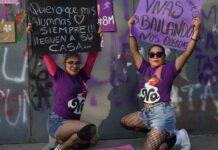 Two protestors wearing purple crouch down and display their placards