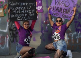 Two protestors wearing purple crouch down and display their placards