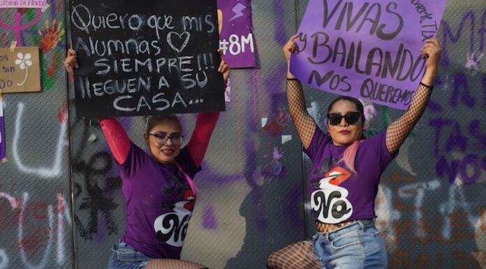 Two protestors wearing purple crouch down and display their placards