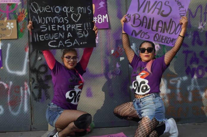 Two protestors wearing purple crouch down and display their placards