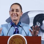 Mexican President Claudia Sheinbaum standing at the presidential podium during her mananera daily press conference. She has both hands raised with palms outward