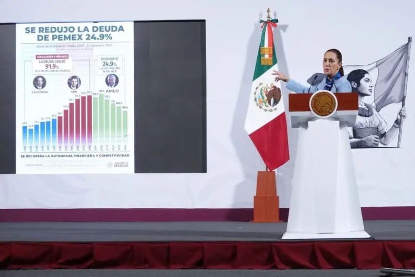 President Claudia Sheinbaum at a press conference pointing to a projection screen with an infographic displaying which recent presidential administrations before hers saw an increase in Pemex's debt amount and which saw a reduction.