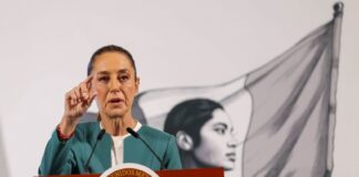 Claudia Sheinbaum at her daily press conference. She is gesturing with her thumb and forefinger to reporters as she speaks in the press briefing room at the National Palace