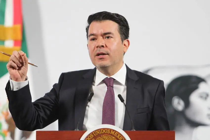 A Mexican man in a suit and tie standing at the presidential podium in Mexico's National Palace's press briefing room.