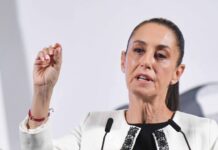 Mexico's President Claudia Sheinbaum standing at the presidential podium and gesturing with her thumb and forefinger as she makes a point during her daily press conference.