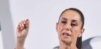 Mexico's President Claudia Sheinbaum standing at the presidential podium and gesturing with her thumb and forefinger as she makes a point during her daily press conference.