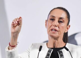 Mexico's President Claudia Sheinbaum standing at the presidential podium and gesturing with her thumb and forefinger as she makes a point during her daily press conference.