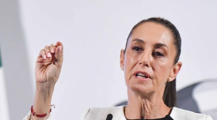 Mexico's President Claudia Sheinbaum standing at the presidential podium and gesturing with her thumb and forefinger as she makes a point during her daily press conference.