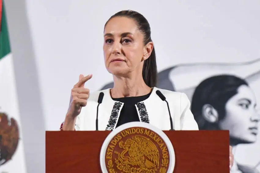 Claudia Sheinbaum standing at the presidential podium in Mexico's National Palace press briefing room. She is gesturing with one finger pointed outward.