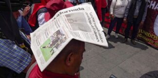 A person shields themself from the sun with a newspaper