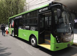 A full-sized public transport bus painted in green and black. It its model name, the Taruk, written in a couple of places on the bus and also the name of one of the designing companies, Mega Flux.