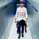 Checo Pérez walks down a hallway after returning from a race, wearing his Red Bull Formula 1 uniform