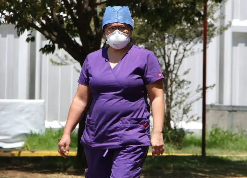 Doctor in purple scrubs walking on the campus of a hospital in Mexico. She is wearing a protective mask.