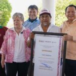 Mexico's Environment Minister, Alicia Barcena, a middle-aged woman with graying hair stands next to an unidentified Mexican man holding a framed enlarged document of certification of Sacpukenha as one of three new Maya protected areas. Around them are other people smiling into the camera.