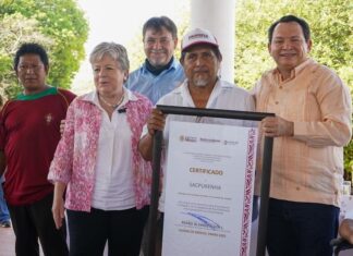 Mexico's Environment Minister, Alicia Barcena, a middle-aged woman with graying hair stands next to an unidentified Mexican man holding a framed enlarged document of certification of Sacpukenha as one of three new Maya protected areas. Around them are other people smiling into the camera.