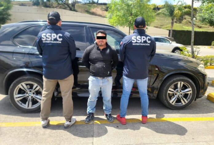 Two police officers with their backs to the camera standing in front of a police sedan. Their jackets say 