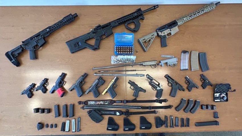 A display of pistols, automatic rifles, ammunition and clips arranged in rows on a table.