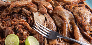 A plate of carnitas served with lime and a fork
