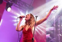 A blonde woman in a red sequined sleevless gown sings her heart out with eyes closed onstage under spotlights and purple projection screens at the Polanco Jazz Festival in Mexico City