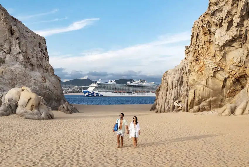 A couple on a Cabo San Lucas beach as a cruise ship passes behind them