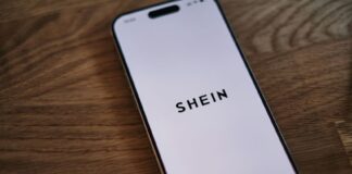 A phone showing the logo of Shein, the Chinese e-commerce app. Wood background