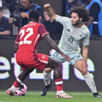 Two soccer players face off, one wearing a red Canadian jersey and the other a white and green Mexican jersey
