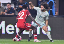 Two soccer players face off, one wearing a red Canadian jersey and the other a white and green Mexican jersey