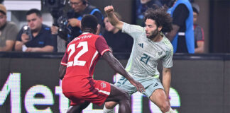 Two soccer players face off, one wearing a red Canadian jersey and the other a white and green Mexican jersey