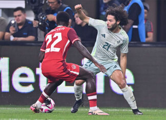 Two soccer players face off, one wearing a red Canadian jersey and the other a white and green Mexican jersey