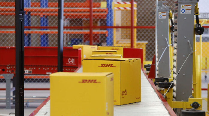 DHL boxes move down a conveyor belt in an industrial facility
