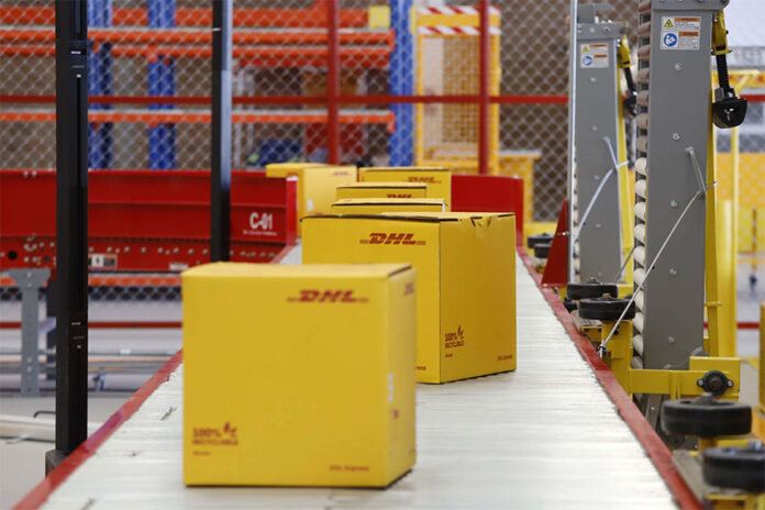 DHL boxes move down a conveyor belt in an industrial facility