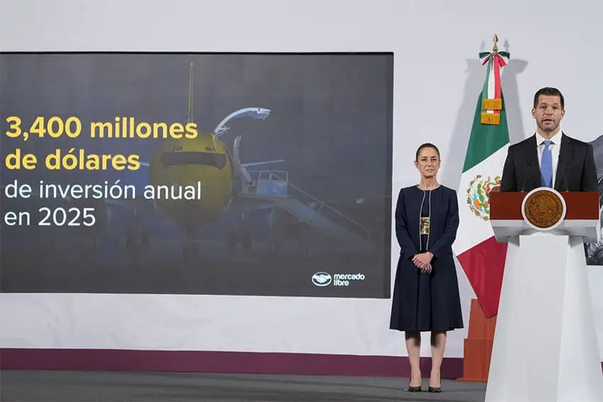 A white man in a suit stands at a podium in front of a screen reading "3.400 millones de dolares de inversion anual en 2025" as Mexican President Claudia Sheinbaum looks on