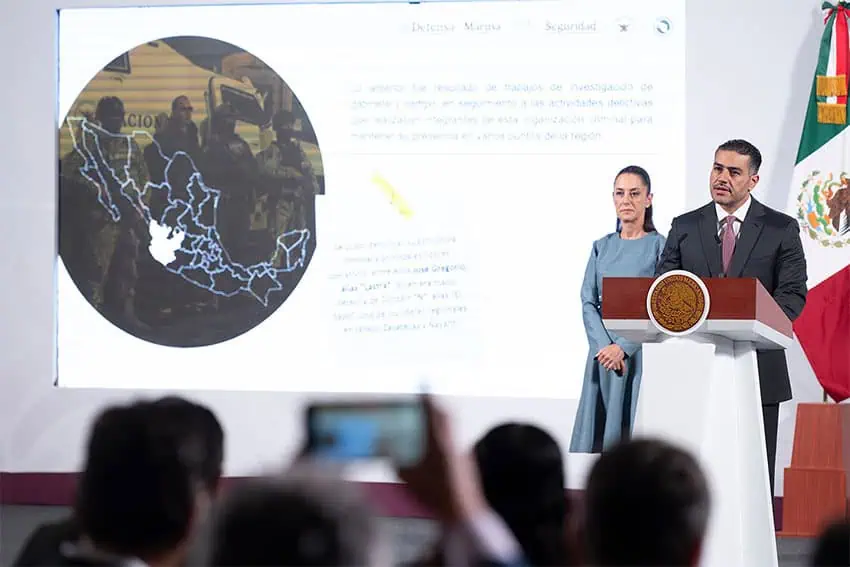 Security Secretary Omar García Harfuch speaks at a podium in front of a map of Jalisco as President Claudia Sheinbaum looks on