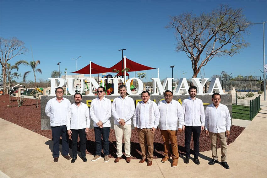 Politicians in white shirts stand in front of a playground and a sign reading "Punto Maya"