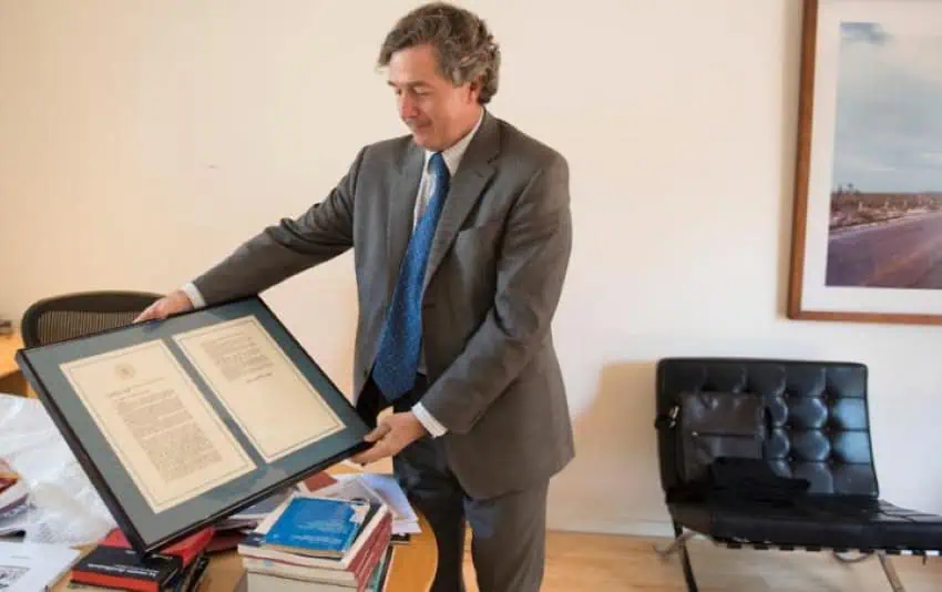 Luis de la Calle holding a framed copy of NAFTA in his office.