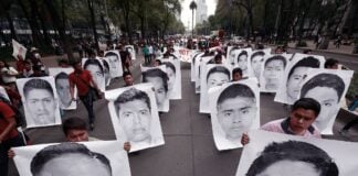 Protesters holding up posters the size of their bodies that show different members of the so-called Ayotzinapa 43 students as they march down a Mexico City street.