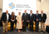 A group of older men and women stand in front of a screen reading OriGen Health Research Center