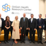 A group of older men and women stand in front of a screen reading OriGen Health Research Center