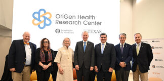 A group of older men and women stand in front of a screen reading OriGen Health Research Center