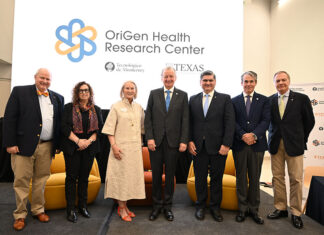 A group of older men and women stand in front of a screen reading OriGen Health Research Center