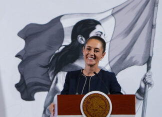 President Claudia Sheinbaum smiles from behind a podium at her morning press conference