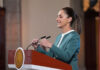 President Claudia Sheinbaum adjusts the microphone as she stands at a podium during her mañanera conference, where she discussed the hacking of her phone