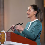 President Claudia Sheinbaum adjusts the microphone as she stands at a podium during her mañanera conference, where she discussed the hacking of her phone