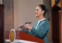 President Claudia Sheinbaum adjusts the microphone as she stands at a podium during her mañanera conference, where she discussed the hacking of her phone