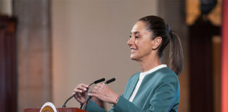 President Claudia Sheinbaum adjusts the microphone as she stands at a podium during her mañanera conference, where she discussed the hacking of her phone