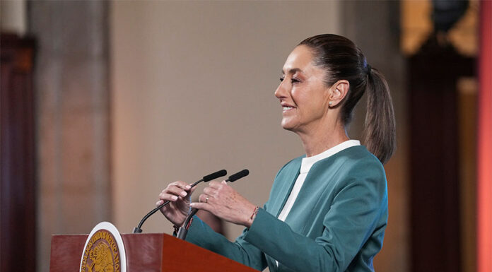 President Claudia Sheinbaum adjusts the microphone as she stands at a podium during her mañanera conference, where she discussed the hacking of her phone