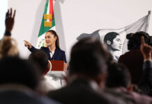 President Sheinbaum, visible at a podium behind a sea of silhouettes, points to the crowd to call on a reporter